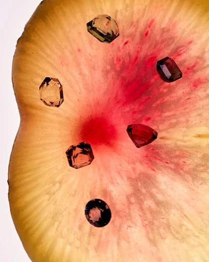 Arrangement of six raw gemstone jewels on a light yellow and red translucent mineral slice, studio lighting, bright color palette.