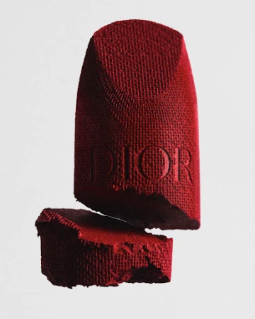 A broken red Dior lipstick on a light grey background, featuring a visible textured surface and embossed lettering.