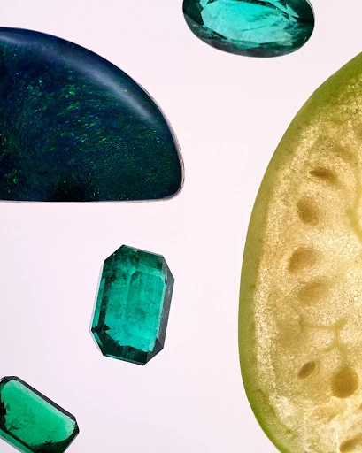 Macro studio shot of gem stones and fruit segment against a white backdrop. The gem stones feature emerald and blue hues.