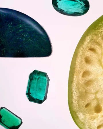 Macro studio shot of gem stones and fruit segment against a white backdrop. The gem stones feature emerald and blue hues.