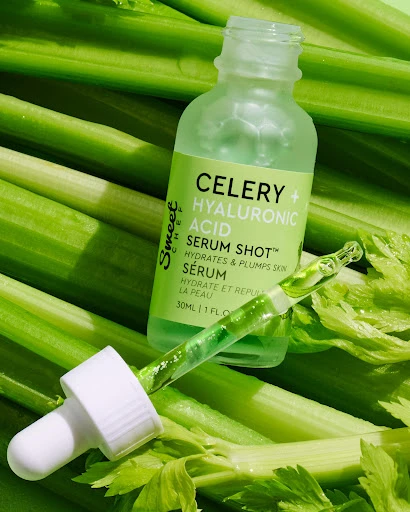 Close-up studio shot of a bottle of celery and hyaluronic acid serum on a bed of fresh celery stalks, with a dropper bottle beside.