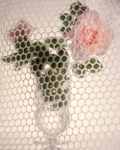 Floral arrangement in a vase, softly visible through a protective bubble wrap layer, creating a textured, blurred aesthetic.