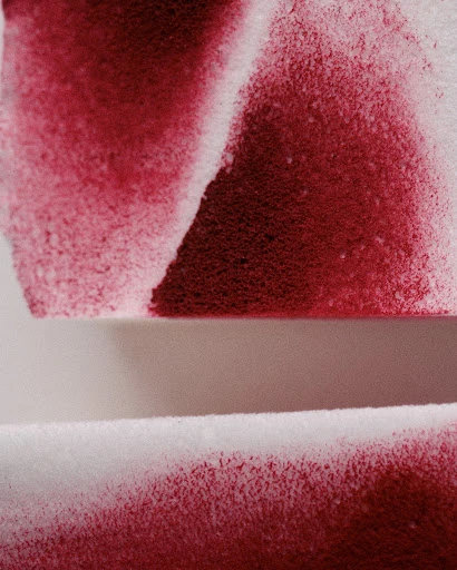 Close-up of white paper or textile material partially covered in red powder or dye, creating an abstract pattern with a textured effect.