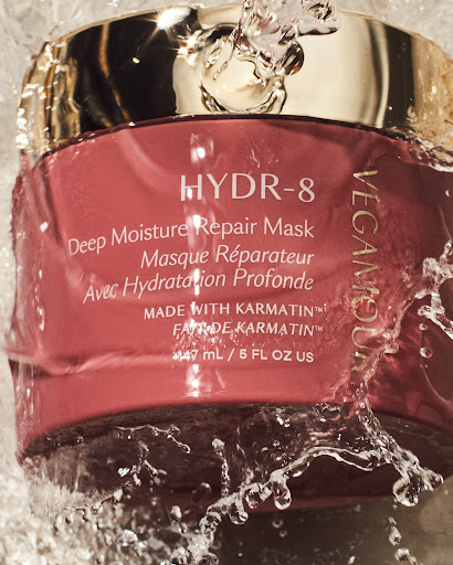Vegamour HYDR-8 Deep Moisture Repair Mask jar with water splashing on it, gold lid and pink container, skincare product shot.