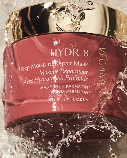 Vegamour HYDR-8 Deep Moisture Repair Mask jar with water splashing on it, gold lid and pink container, skincare product shot.