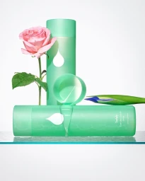 Green cosmetic bottles arranged on a surface with a pink rose and a blue flower against a clean white background