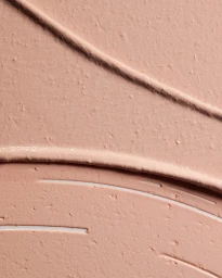 Close-up macro view of thick peach-colored cosmetic cream texture with distinct sweeping curved ridges and fine particulate grains