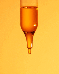 Glass dropper holding amber liquid with a single droplet forming at the tip against a warm yellow background.