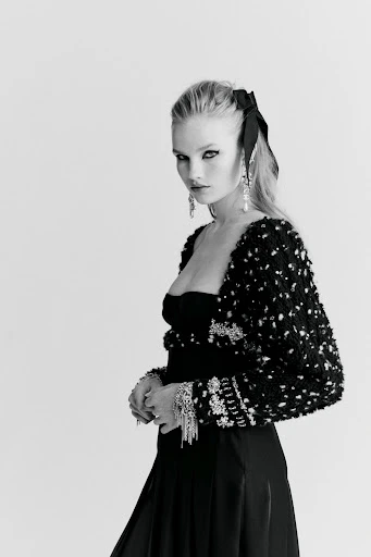 Black and white portrait of an adult woman in elegant black evening wear with decorative jacket, jewelry, and a large hair bow.