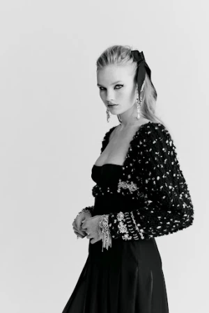 Black and white portrait of an adult woman in elegant black evening wear with decorative jacket, jewelry, and a large hair bow.