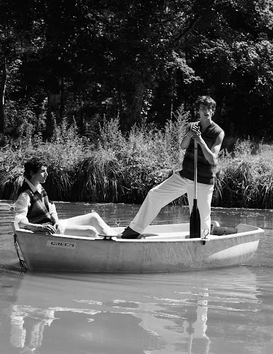 Monochrome photo of a man and woman in a boat on a river, surrounded by lush foliage, creating a vintage and serene atmosphere.