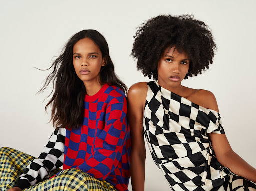 Two dark-skinned adult fashion models wearing vibrant checkered print clothing, posing in front of a clean white backdrop in a studio setting.