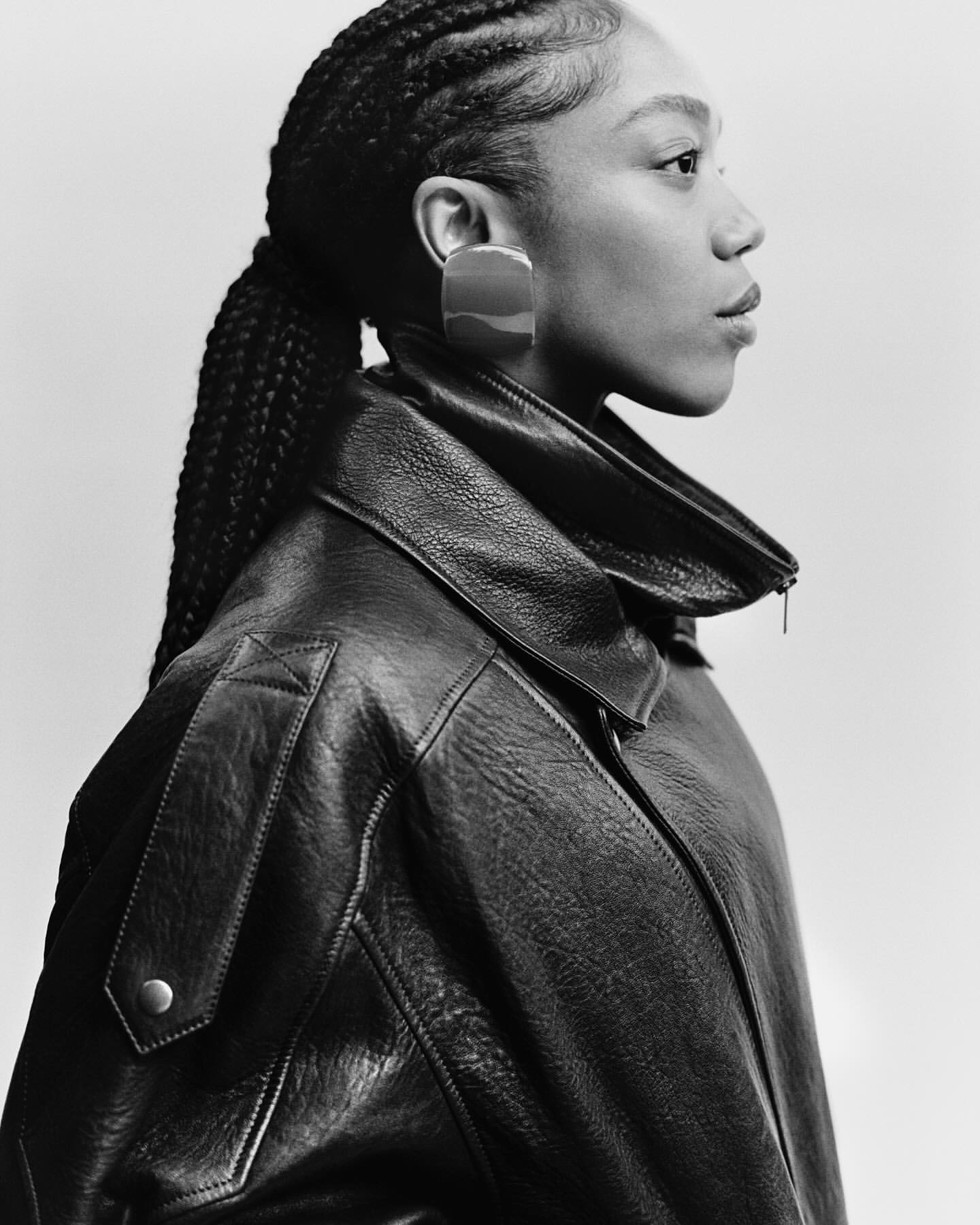 Profile portrait of a Black woman in a black leather jacket and large square earring, captured in monochrome by Luca Campri.