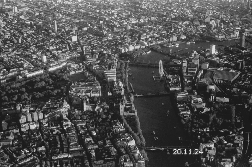 High-angle, black and white aerial photograph of London, showcasing the Thames River, bridges, buildings, parks, and urban architecture in detail.
