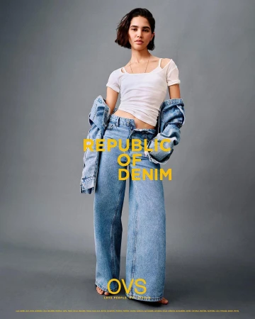 A woman models denim wide-leg jeans and a white tee shirt with a denim jacket hanging off her shoulders in a fashion shot.