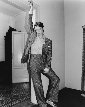 Model in patterned suit and light shirt posing with arm raised inside a room by photographer Luca Campri
