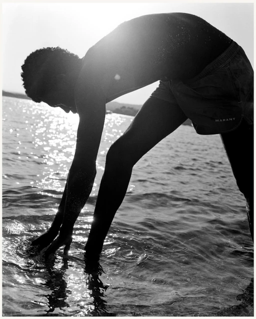Monochrome shot of a man wading in the ocean, captured from a low angle with lens flare obscuring the horizon, highlighting the water.