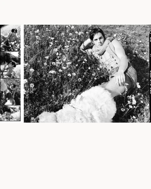 Black and white portrait of a man lying in a field of flowers, with a dog laying next to him on a sunny day in a rural environment.