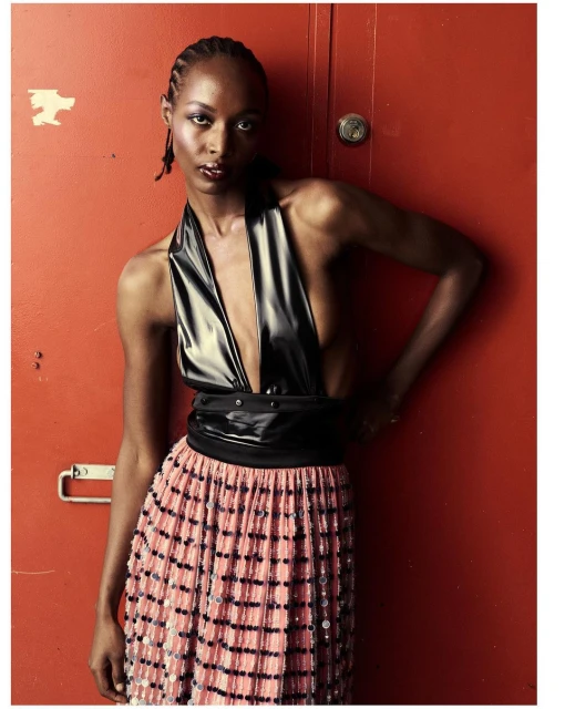Fashionable Black woman in a black top and colorful sequined skirt poses confidently against a red door, looking directly at the camera.