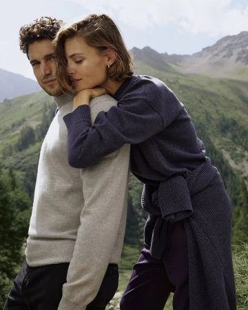 Man in a light grey turtleneck and woman in a navy sweater posing outdoors against a mountain background by photographer Luca Campri