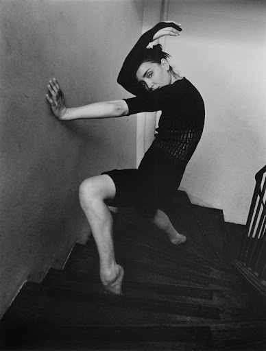 Black and white portrait of a woman in a black dress posing dynamically on an indoor wooden staircase