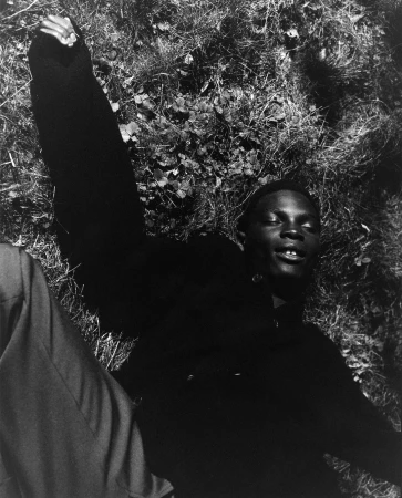 Black man lying on grass with raised arm shot from above in high contrast monochrome by Luca Campri