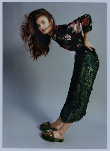 Woman in floral blouse and green fringed skirt posing against a grey studio backdrop by Luca Campri
