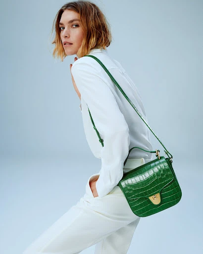 Woman in white outfit posing with a green crocodile-texture crossbody bag in a studio setting, fashion photography for e-commerce.