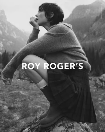 Monochrome fashion portrait of a woman crouching outdoors in a knit sweater and plaid skirt by photographer Luca Campri