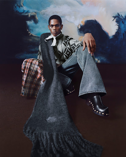 Young adult posing with scarf and stylish clothing against a painterly blue backdrop in a studio fashion shot, high-fashion, eye-level view.