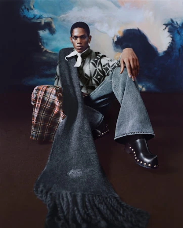 Young adult posing with scarf and stylish clothing against a painterly blue backdrop in a studio fashion shot, high-fashion, eye-level view.