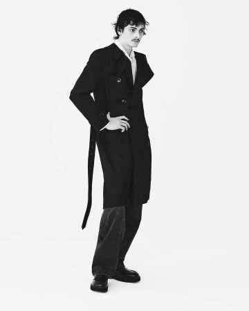 Monochrome fashion portrait of a man wearing a dark trench coat against a white seamless background