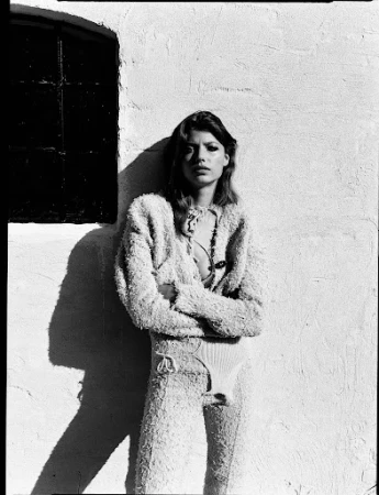 Black and white portrait of a woman wearing a textured fuzzy two piece outfit leaning against a textured exterior wall.