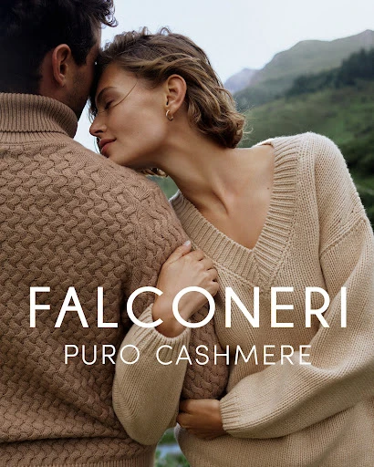 Fashion shot of a couple in beige cashmere sweaters embracing in front of a mountain landscape. The brand name, Falconeri, is visible.