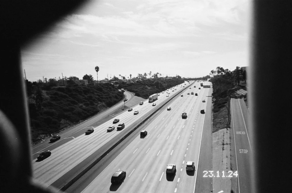 High-angle black and white view of a multi-lane highway filled with cars, captured through a blurred frame, under a bright sky.
