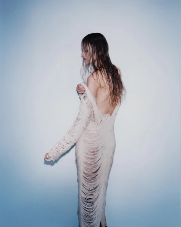 Back view of a woman in a fringed dress against a gradient blue and white background in a studio setting with soft lighting.