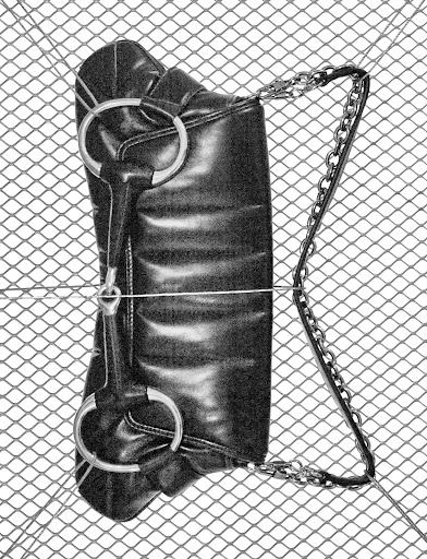 Elevated shot of a black faux-leather handbag with silver chain handle, resting on a diamond-patterned wire mesh.