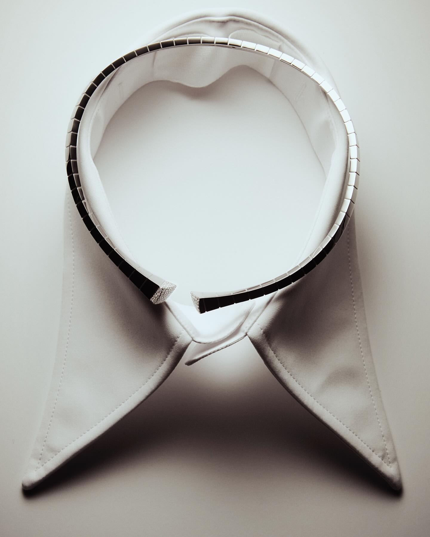 Isolated white detachable shirt collar with dark trim and metal embellishments, flat lay on a white surface. Studio shot with diffused light.