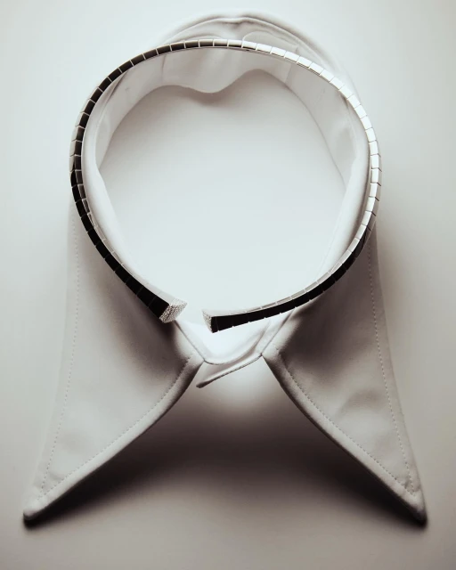 Isolated white detachable shirt collar with dark trim and metal embellishments, flat lay on a white surface. Studio shot with diffused light.