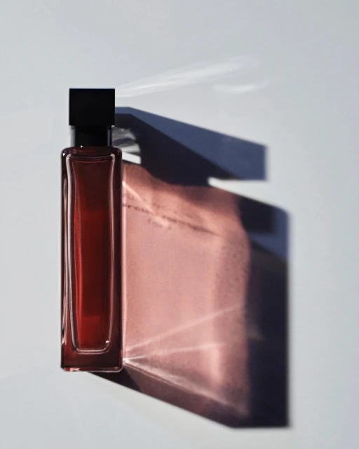 A rectangular perfume bottle with dark liquid stands out against a bright white background with a bold shadow.