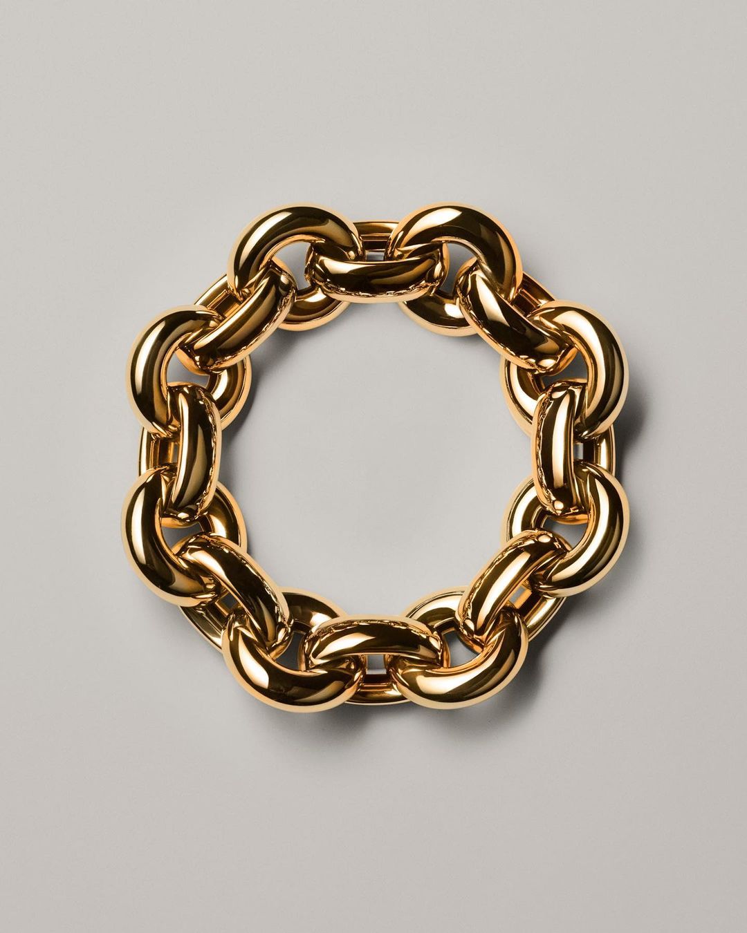 Close-up studio shot of a circular golden chain necklace on a gray surface, jewellery, gold metal with reflective light, fashion concept.