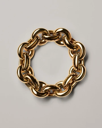 Close-up studio shot of a circular golden chain necklace on a gray surface, jewellery, gold metal with reflective light, fashion concept.