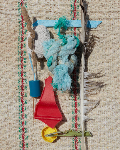 Abstract still life featuring colorful textile and found objects: rope, feather, plastic parts, fiber.
