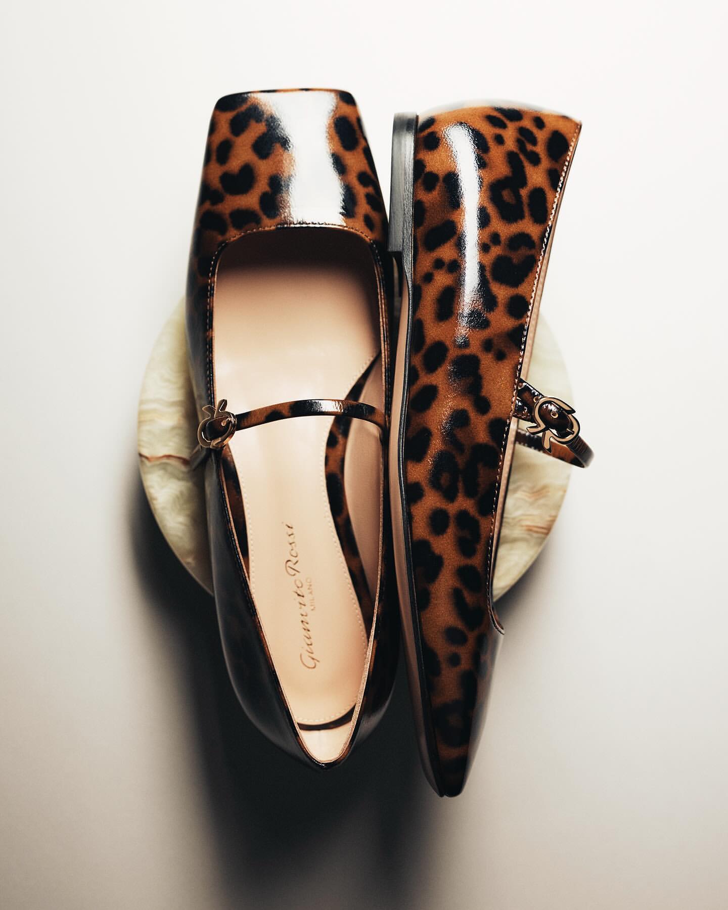 Elevated view of women's Mary Jane shoes featuring a leopard print design, positioned on a marble stand against a bright background.