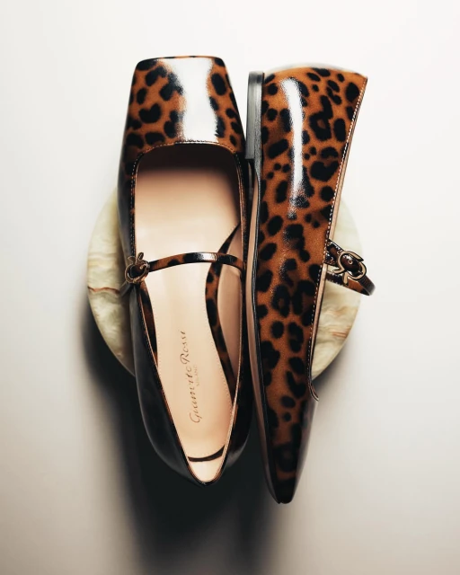 Elevated view of women's Mary Jane shoes featuring a leopard print design, positioned on a marble stand against a bright background.