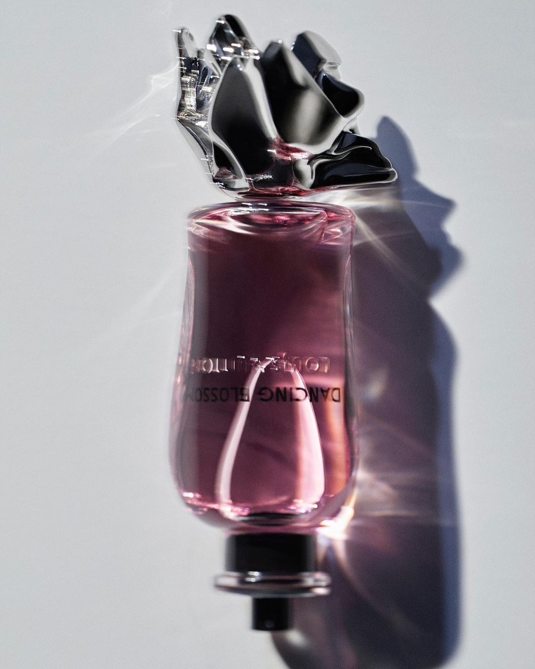 Elegant pink perfume bottle with a silver floral cap on a white background, showcasing its sleek design and presentation.