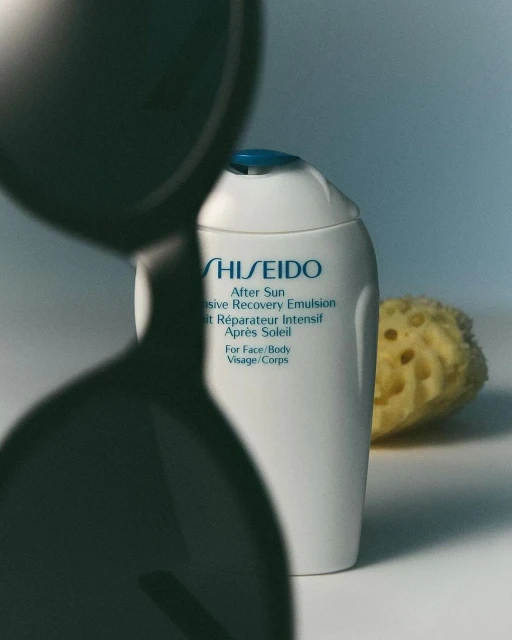 Shiseido After Sun Intensive Recovery Emulsion bottle is showcased alongside a sea sponge, partially obscured by a dark hourglass.