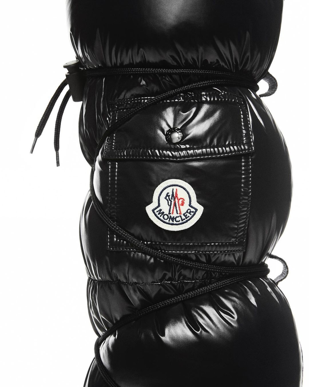 Close-up of black puffy snow boots with black laces and Moncler logo, set against a white background, shiny, puffy texture.