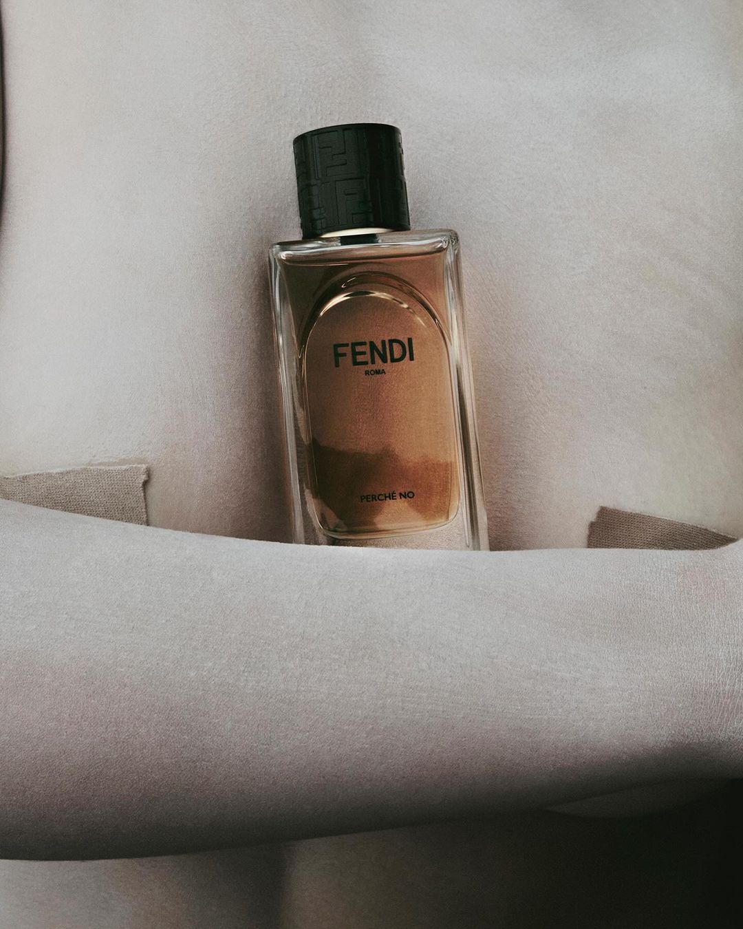 Fendi perfume bottle held closely against bare human skin by folded arms in a close-up shot.