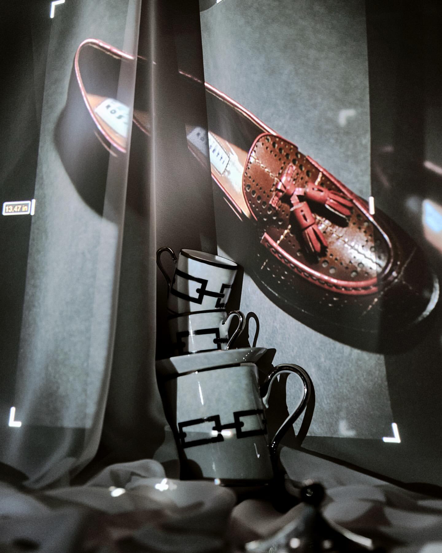 Artistic display of a brown leather loafer with tassels alongside a stack of teacups, creatively positioned against a textured backdrop.